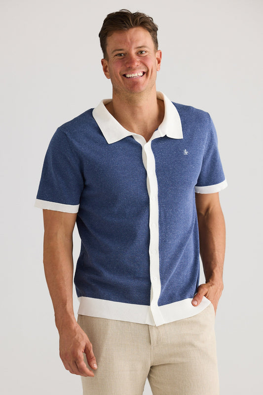Man wearing a blue and white polo shirt with beige pants on a plain background