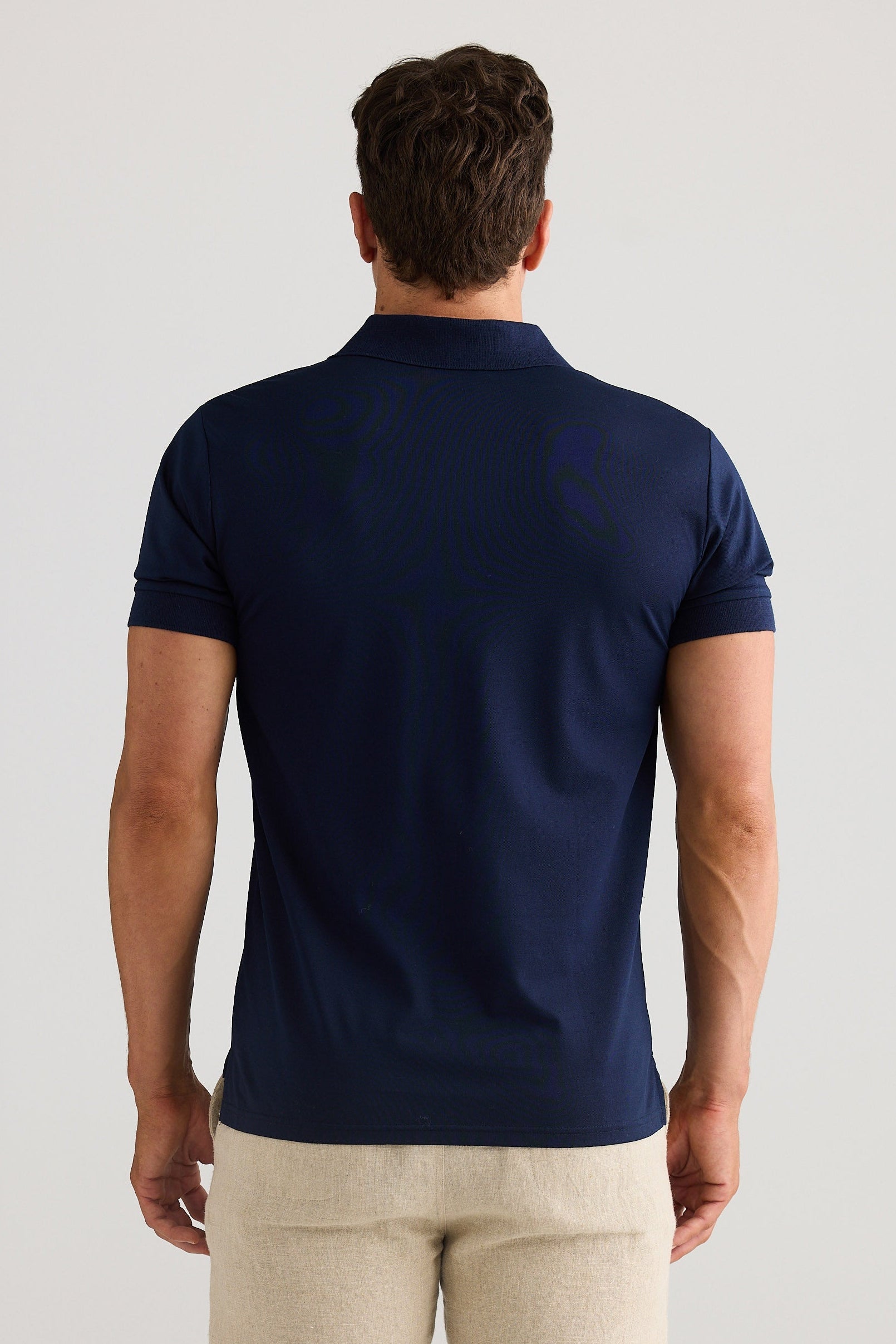 Man wearing a navy blue polo shirt and beige pants on a light gray background