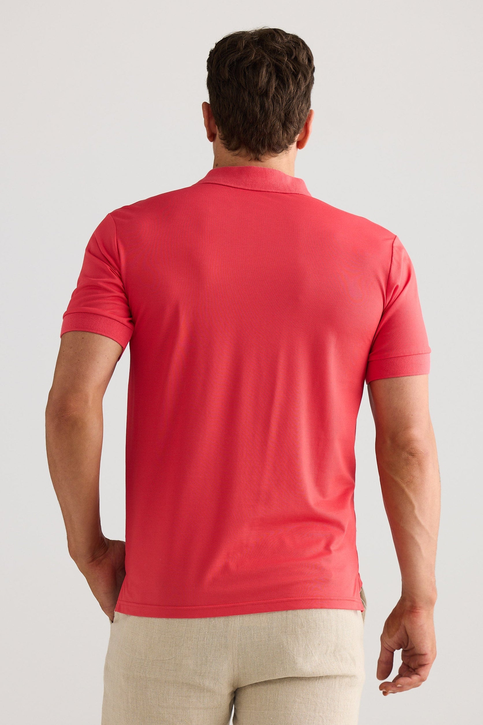 Man wearing a red polo shirt and beige pants against a light gray background