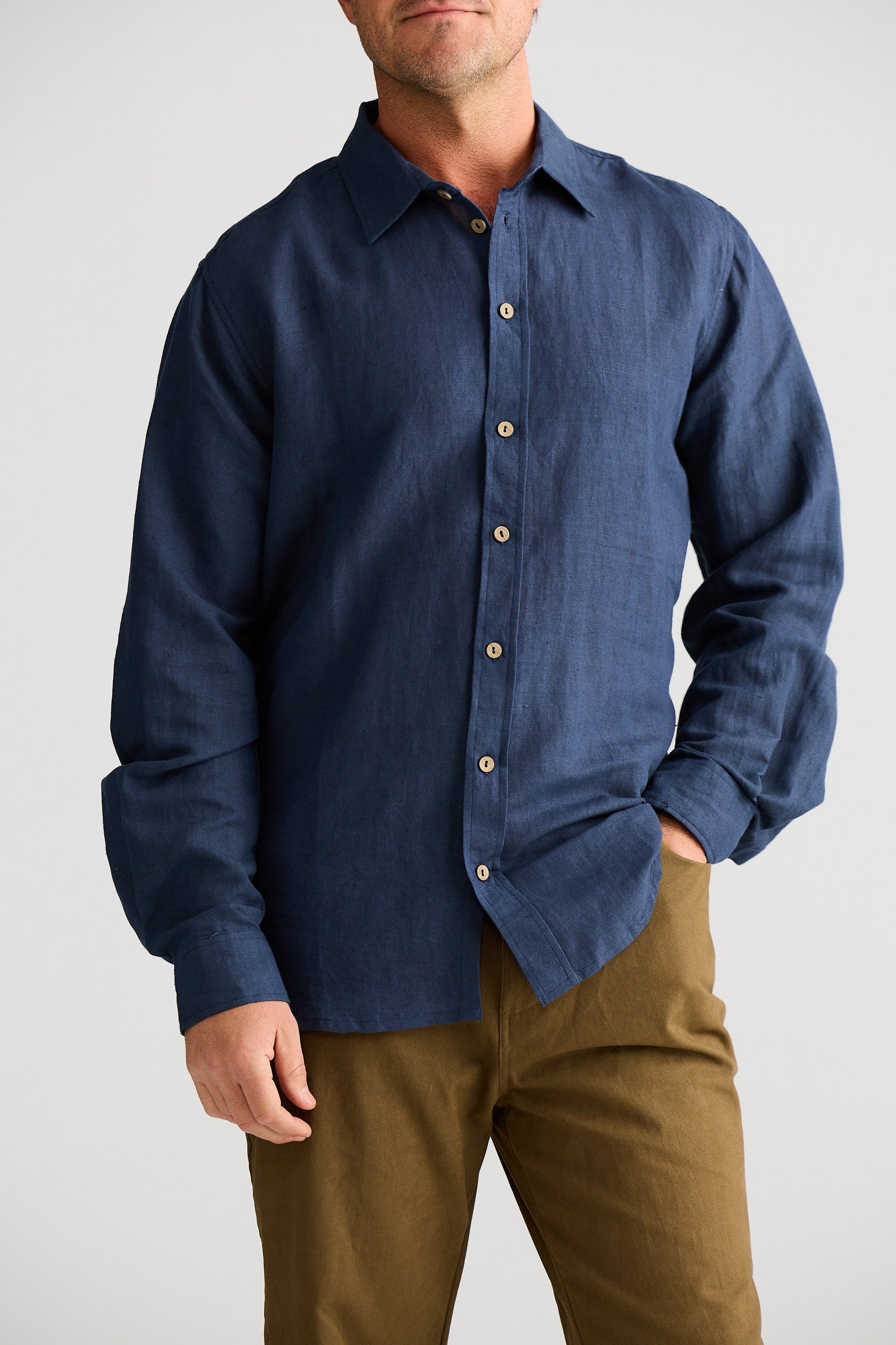 Man wearing a blue button-up shirt and brown pants on a white background