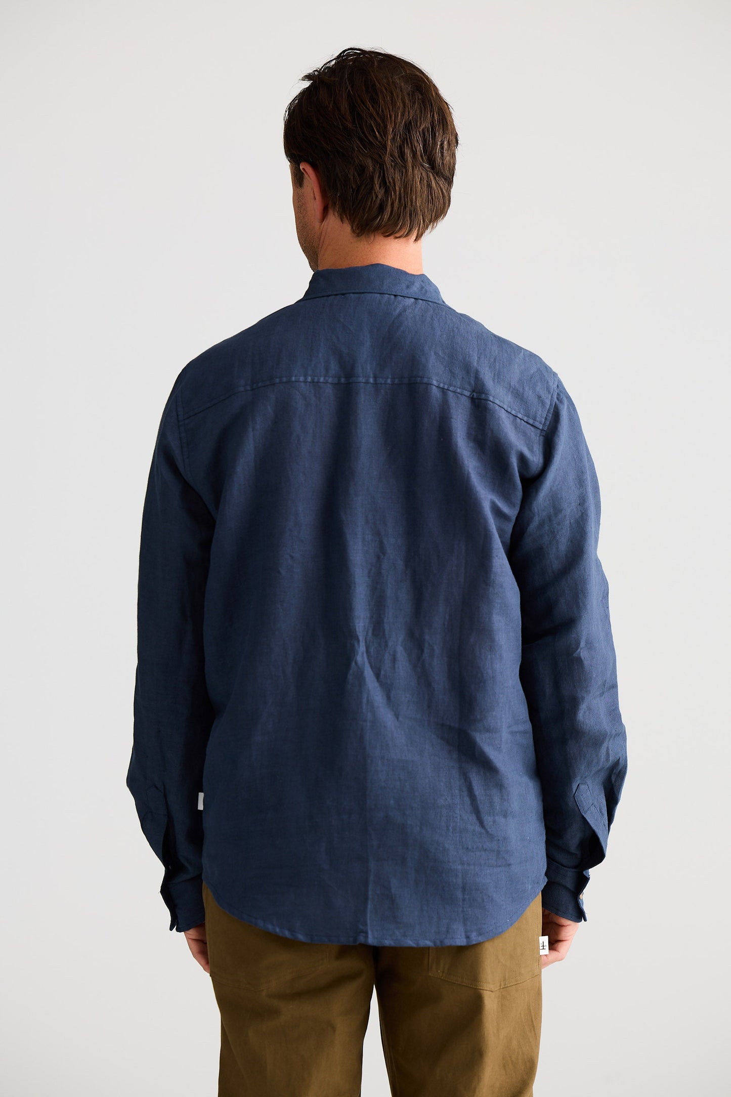Person wearing a blue shirt and brown pants against a white background