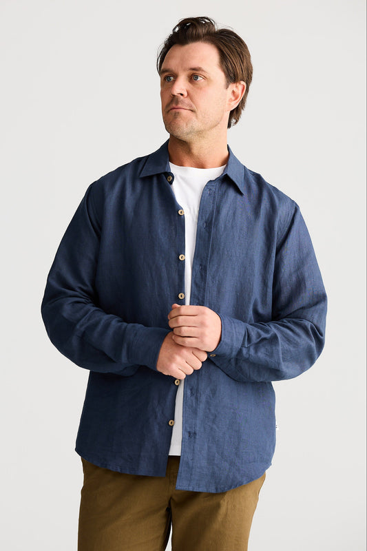Man wearing a blue shirt over a white shirt with brown pants on a light gray background