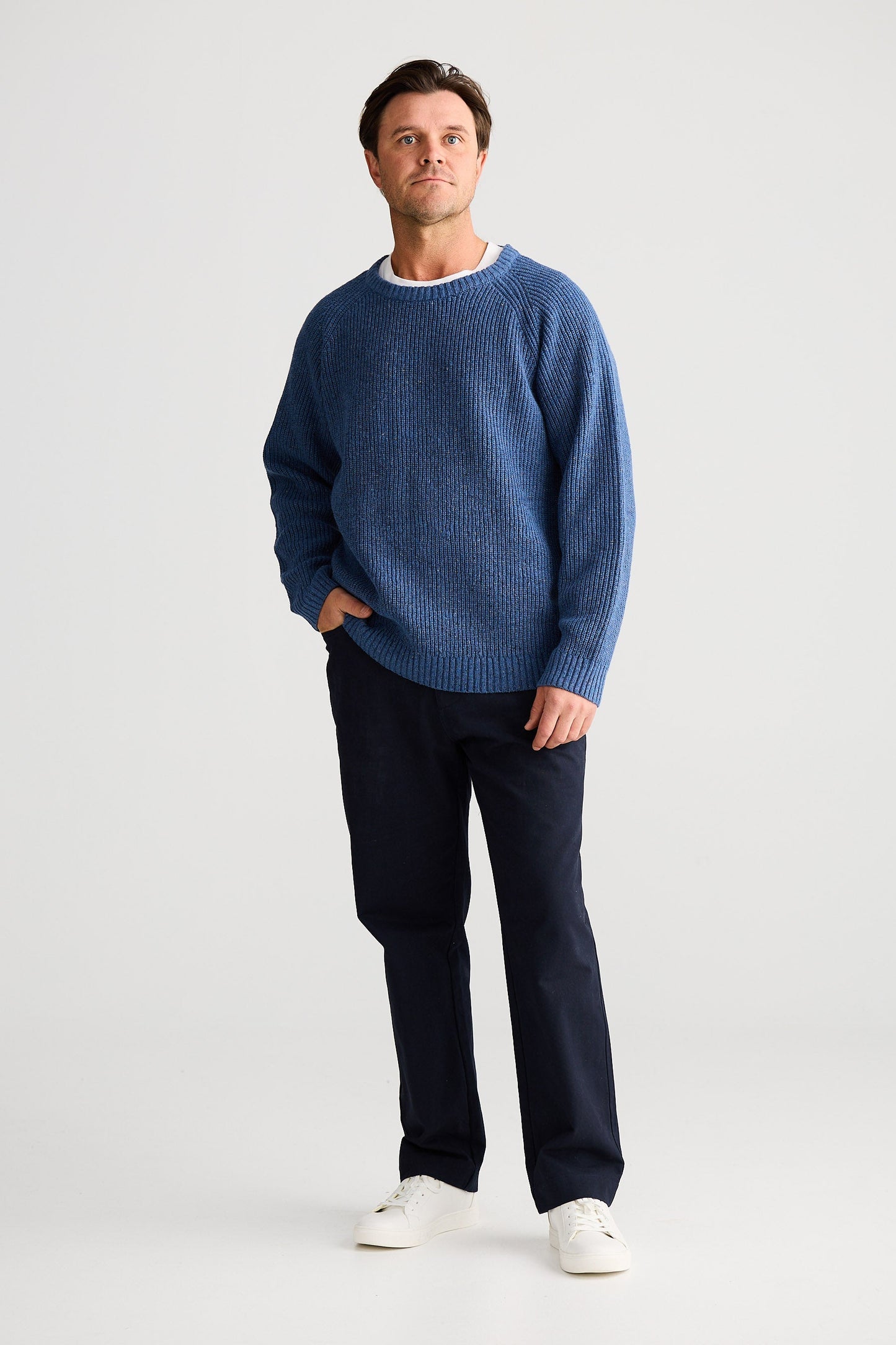 Man wearing a blue sweater and dark pants on a white background