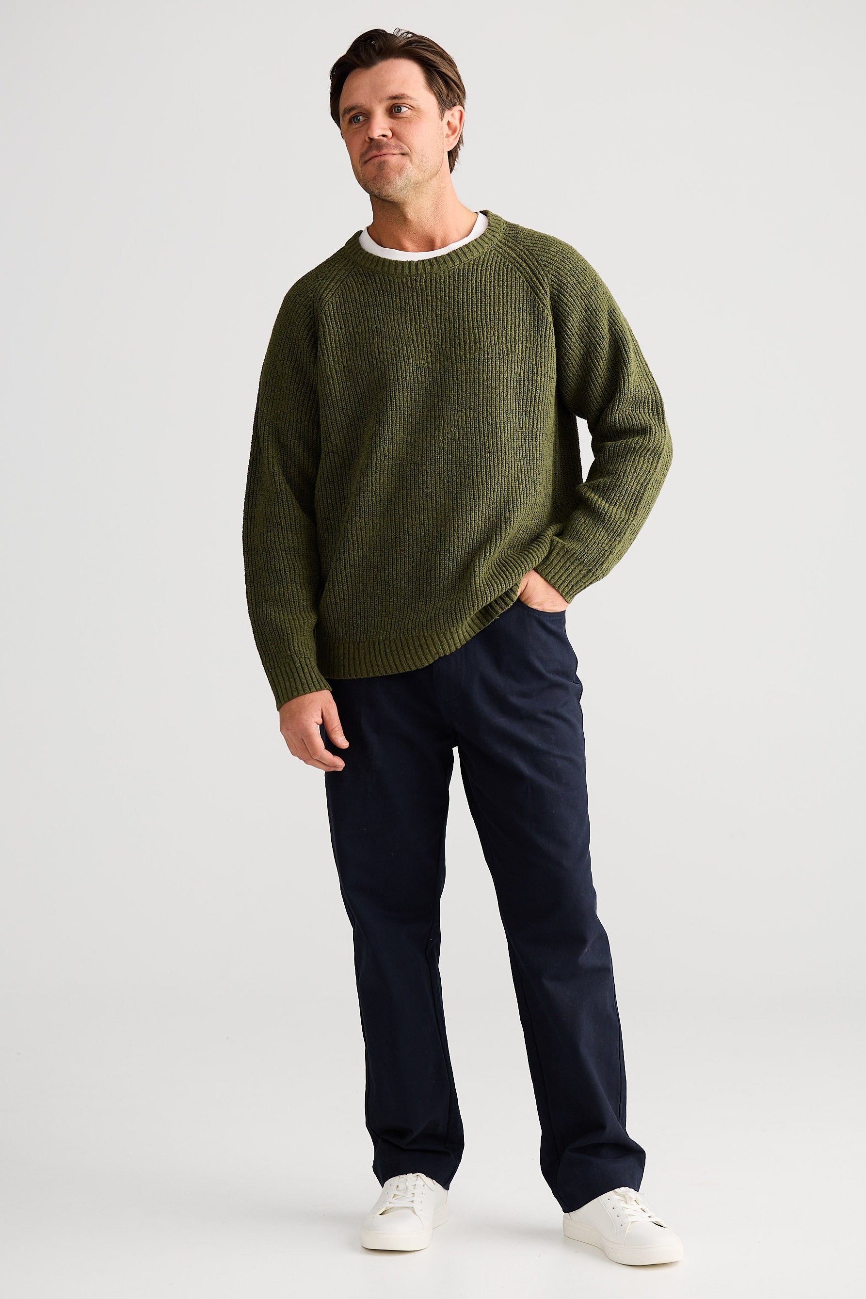Man wearing a green sweater and dark pants on a white background