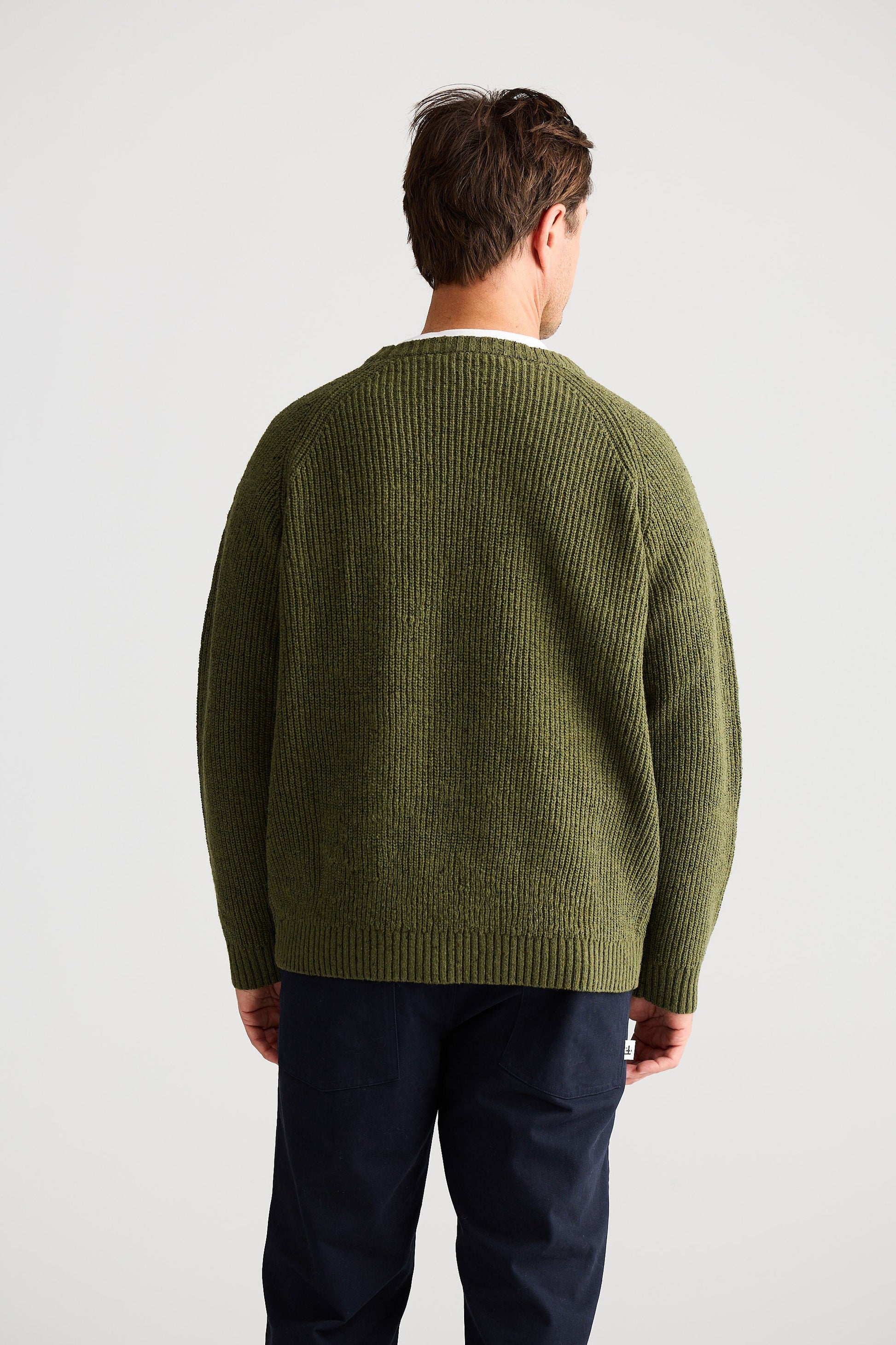 Man wearing a green sweater and dark pants on a light gray background
