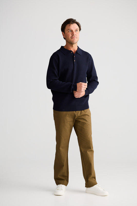 Man wearing a navy polo shirt and brown pants on a white background