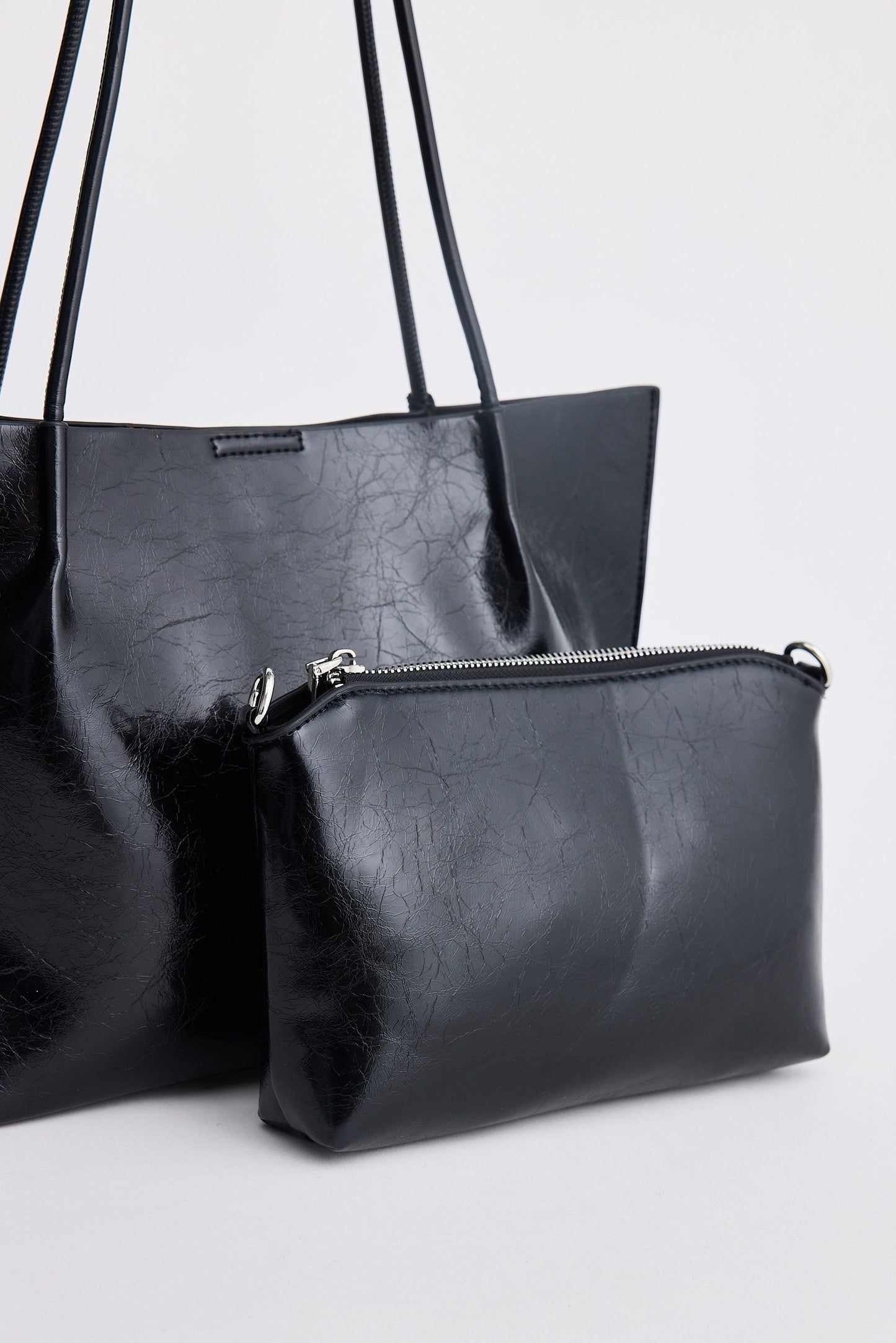 Black leather handbag with a smaller matching pouch on a light gray background