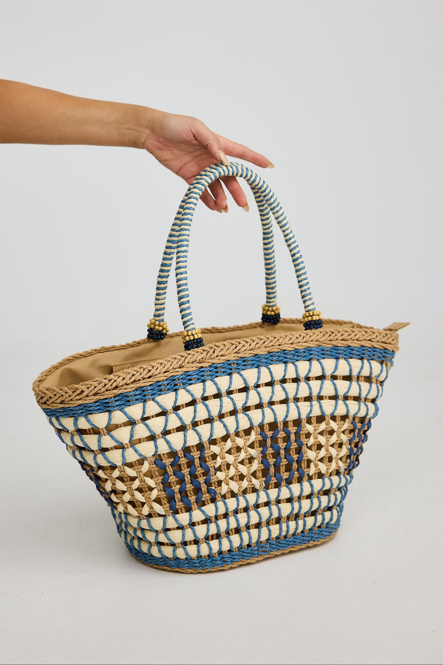 Woven basket with striped handles held by a person against a plain background