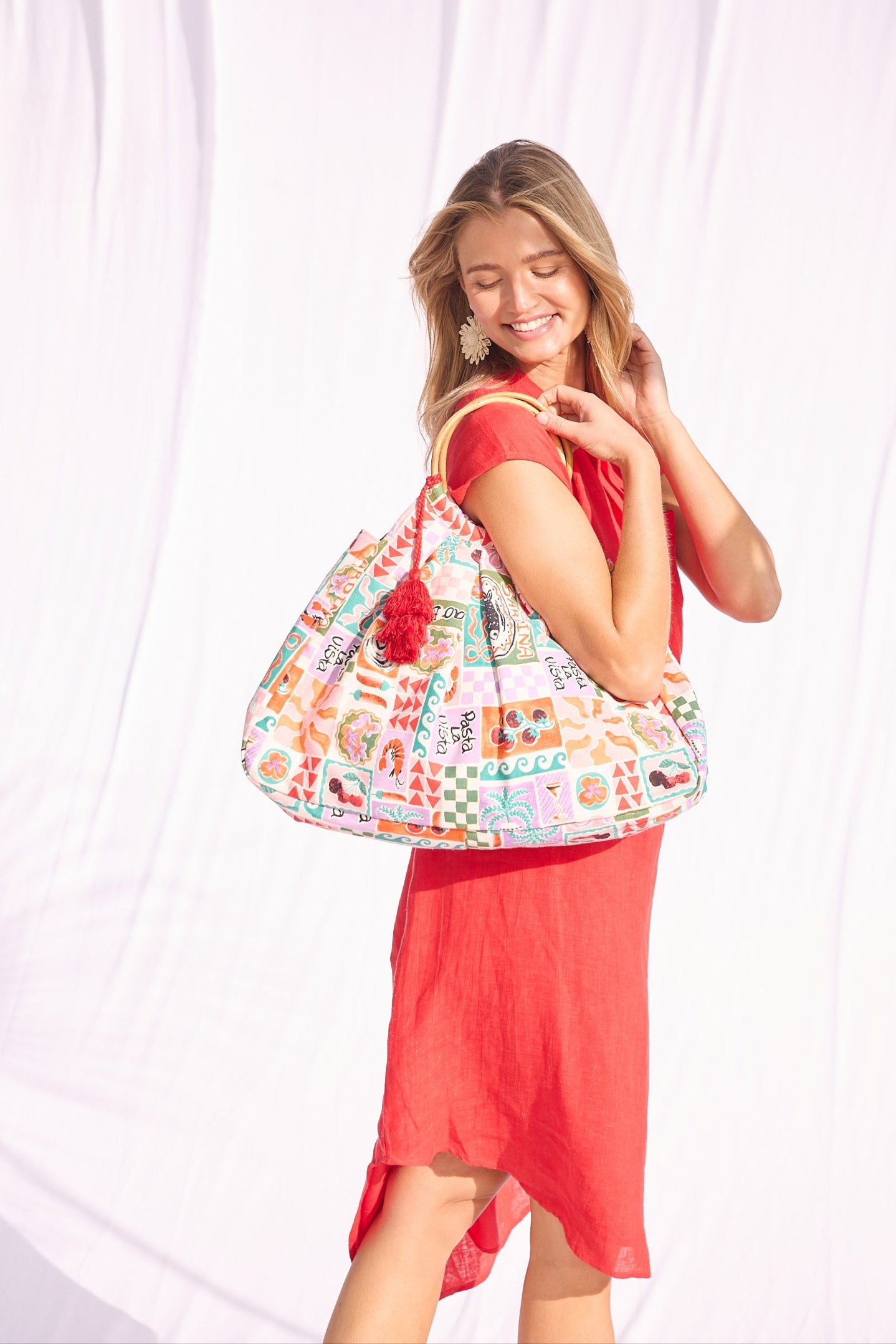 Woman in a red dress holding a colorful patterned bag against a white curtain.