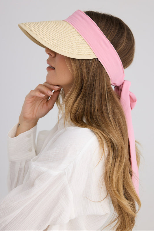 Woman wearing a beige sun visor with a pink ribbon on a plain background