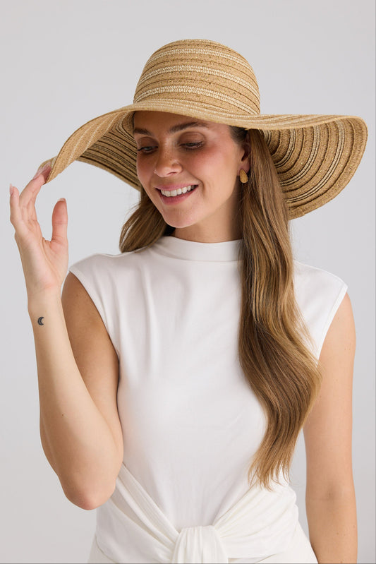 Woman wearing a wide-brimmed straw hat against a plain background