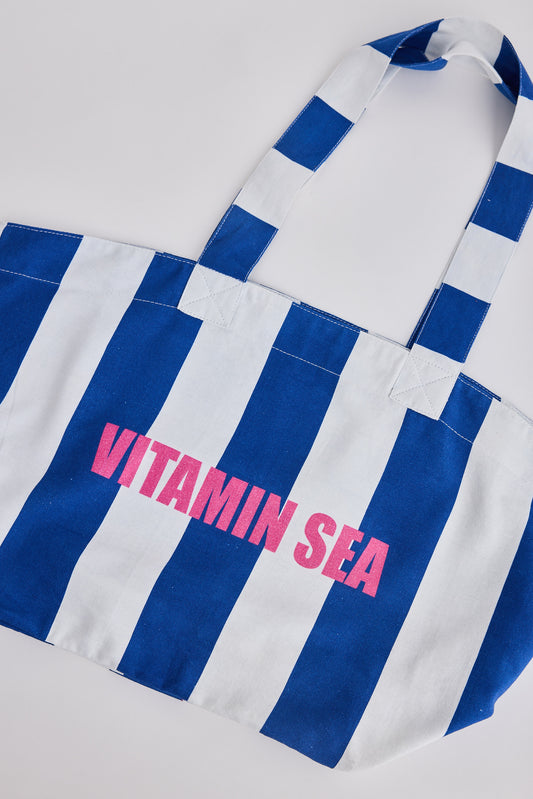 Blue and white striped tote bag with 'Vitamin Sea' text on a light gray background