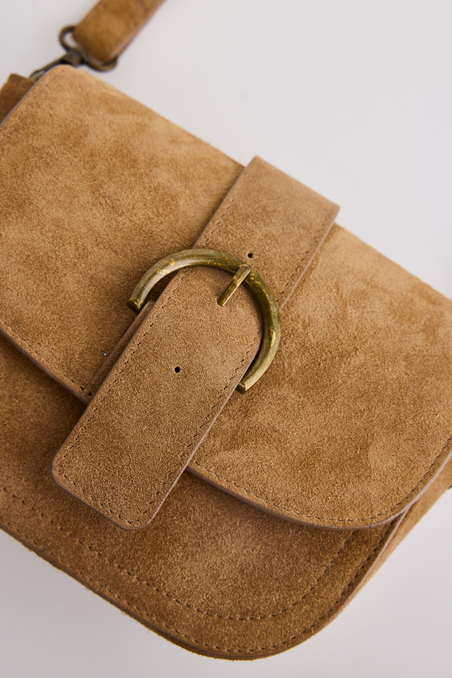 Brown suede handbag with a gold buckle on a light gray background