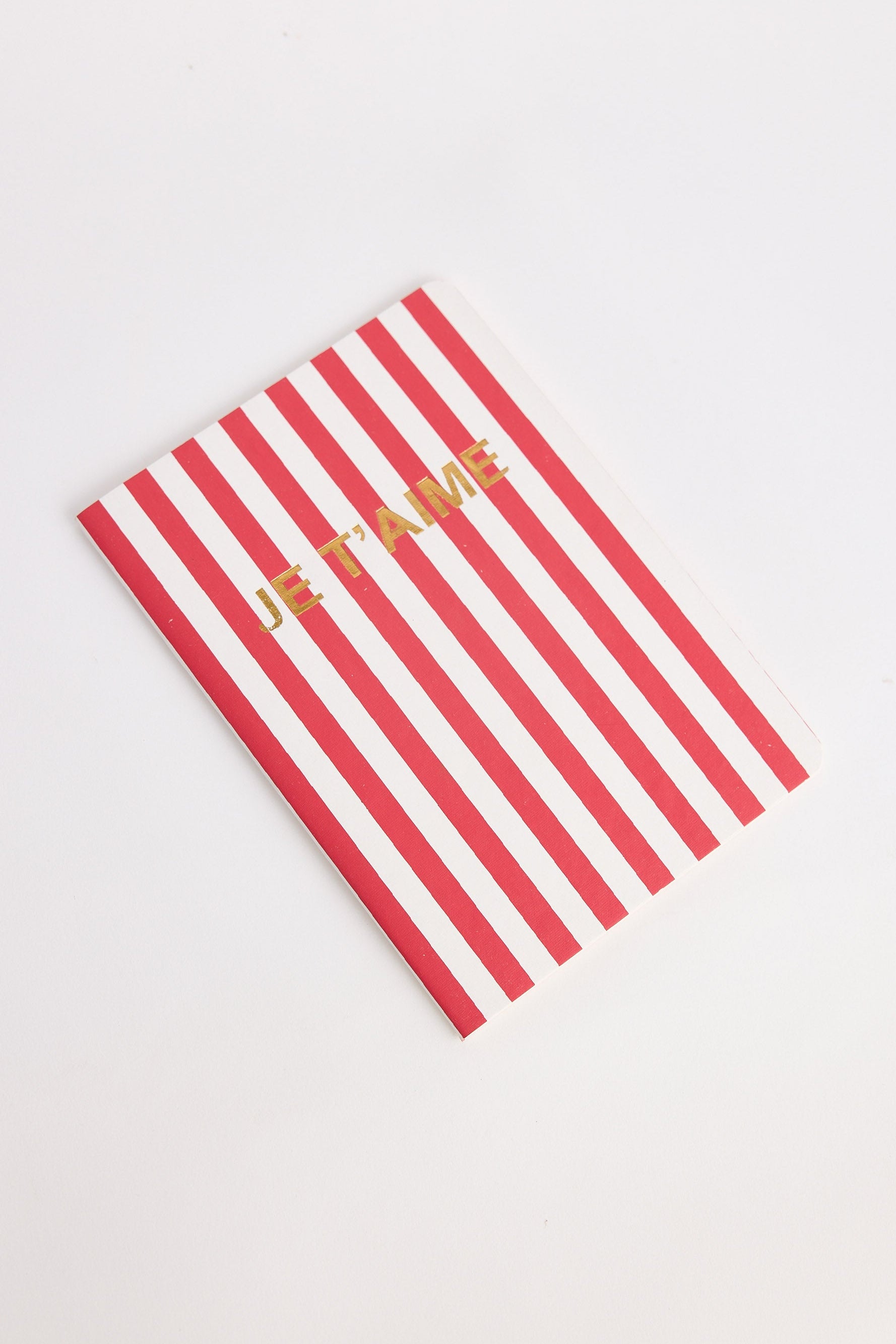 Red and white striped notebook with 'Je t'aime' text on a light gray background