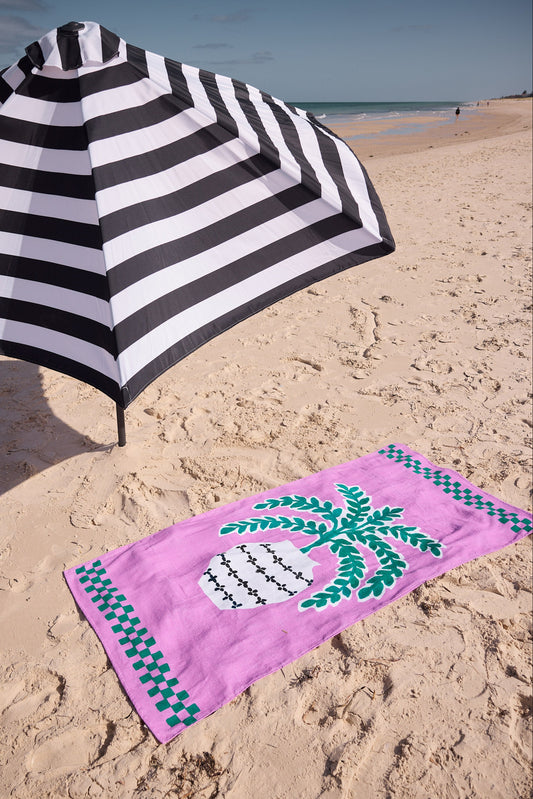 Black and white striped beach umbrella and pink towel with palm tree design on sandy beach