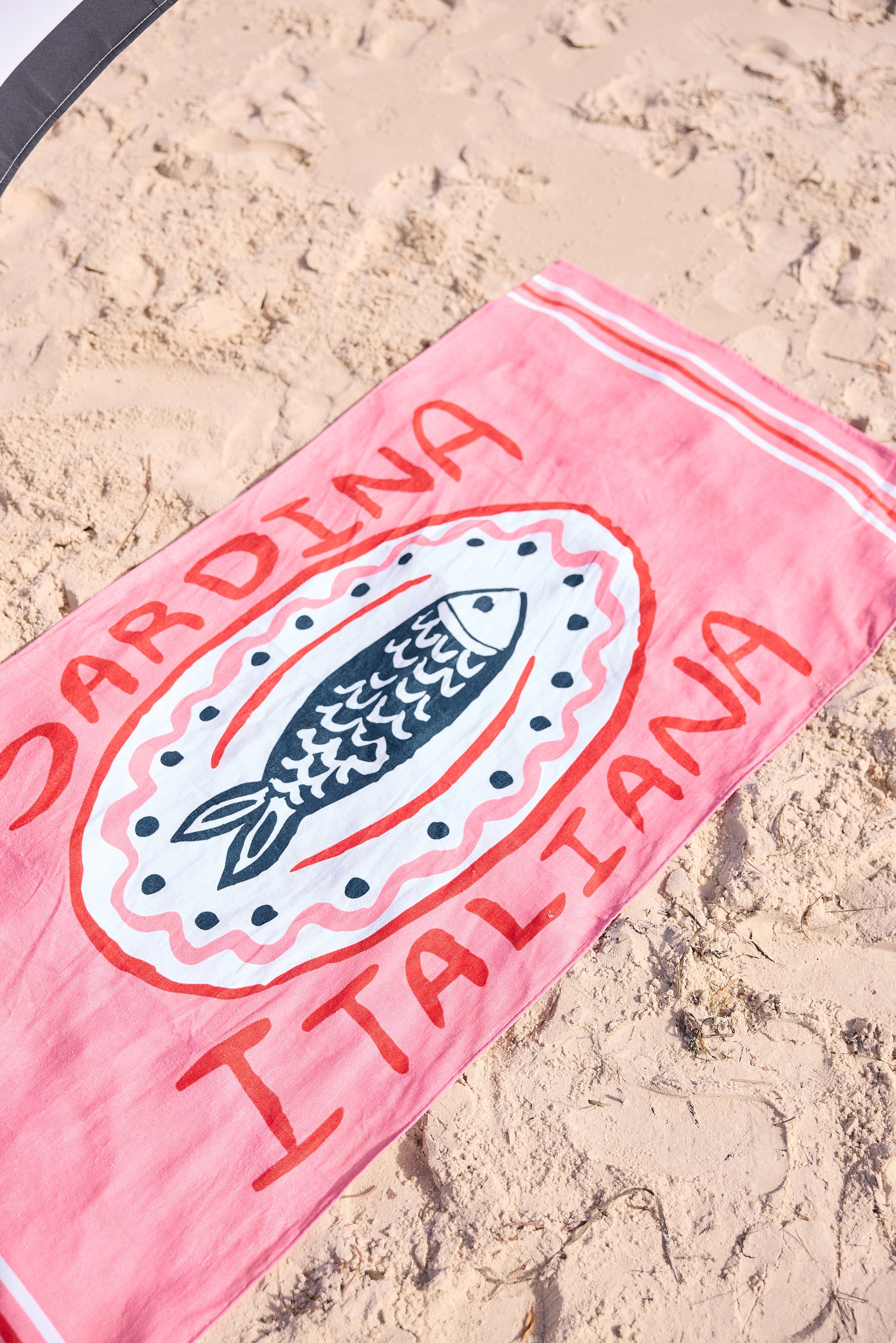 Pink beach towel with fish design and text on sand