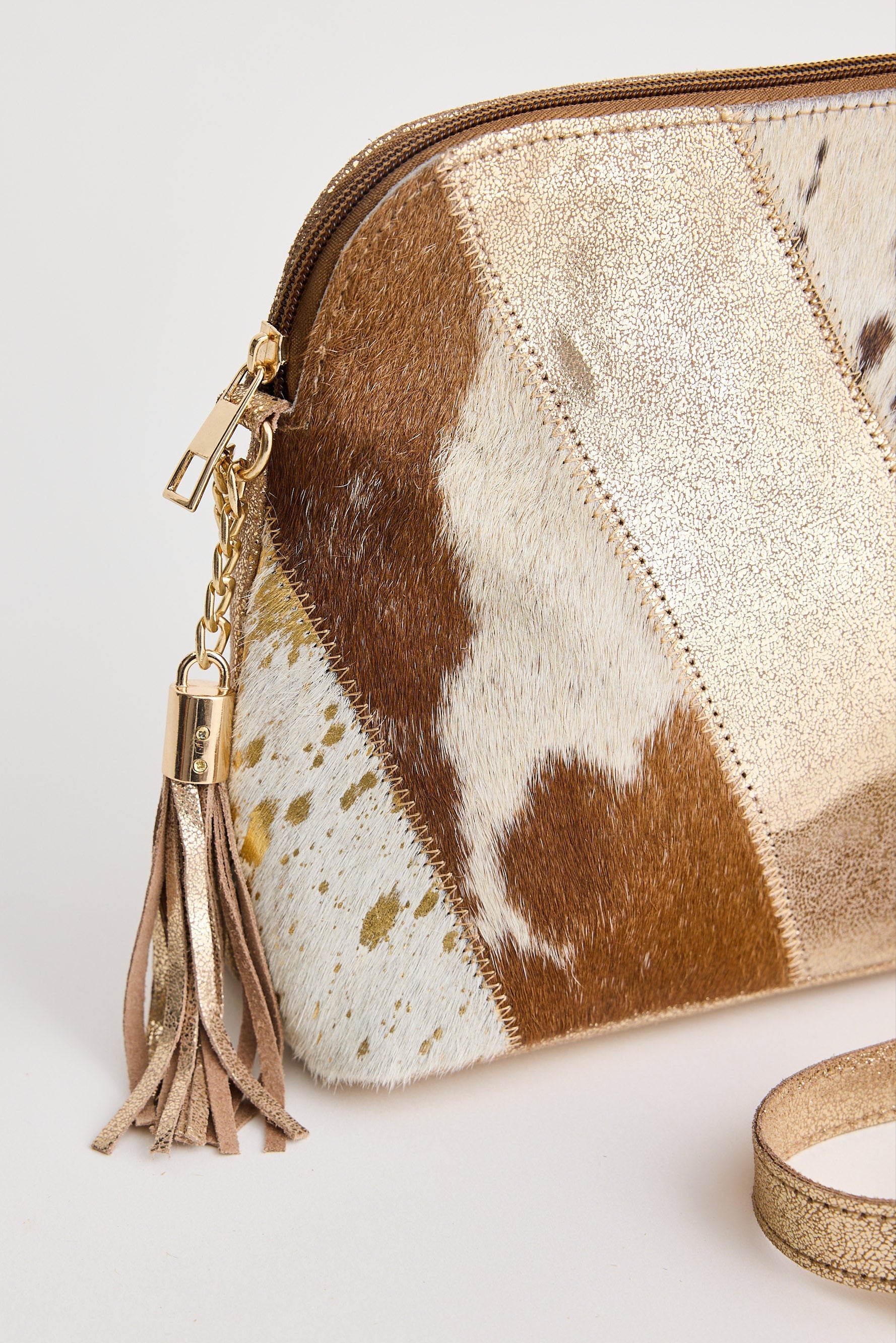 Purse with cowhide leather pattern and gold tassel on a light background