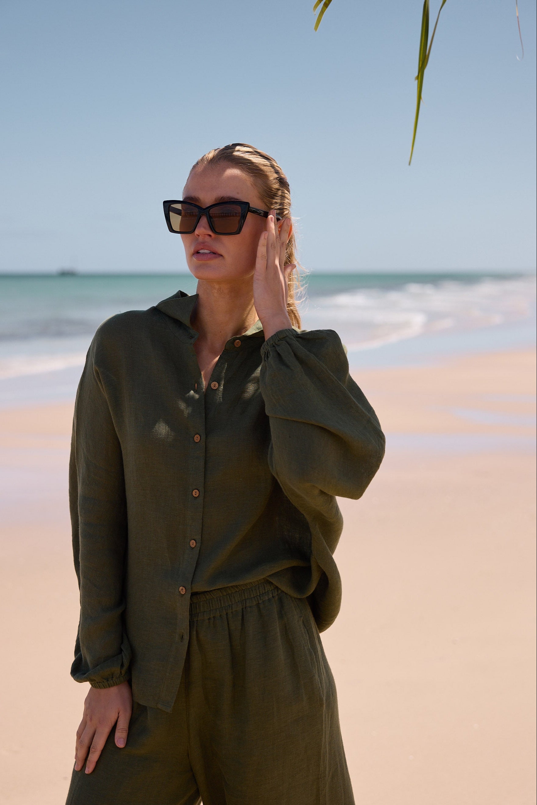 Woman in olive green outfit on a beach with sunglasses