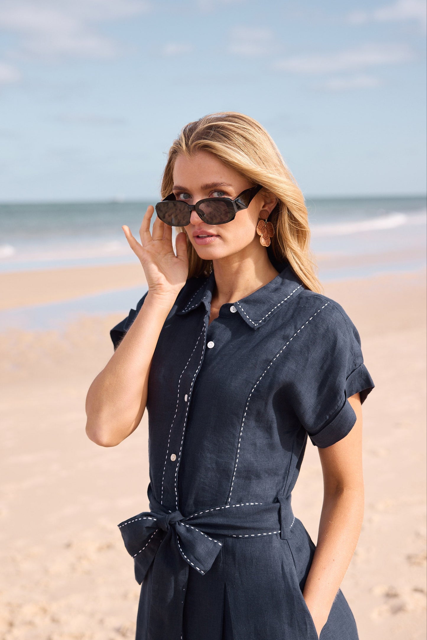 Woman in a navy dress standing on a beach with sunglasses