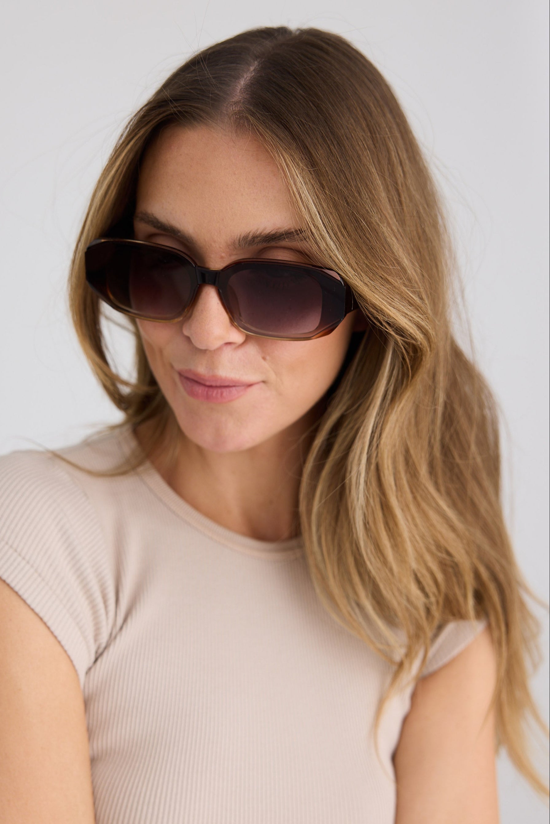 Woman wearing sunglasses and a beige top against a white background