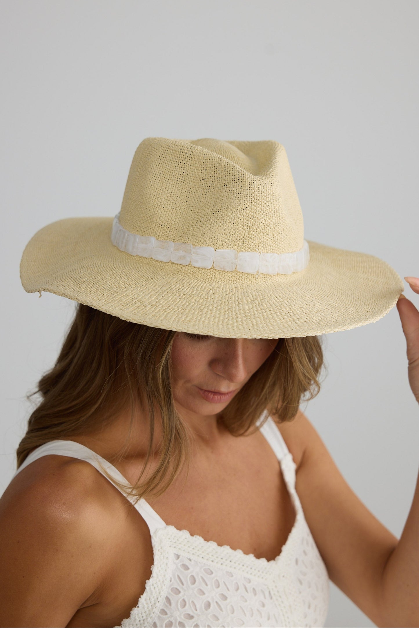 Woman wearing a beige straw hat with a white band on a plain background