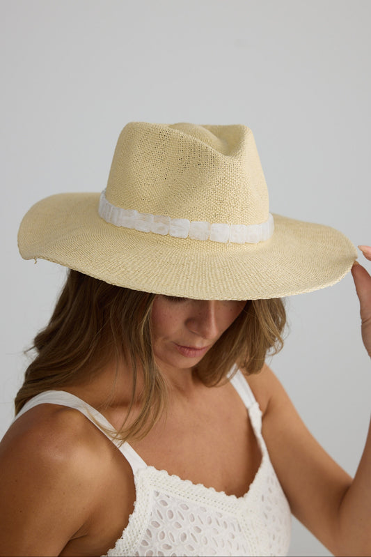 Woman wearing a beige straw hat with a white band on a plain background