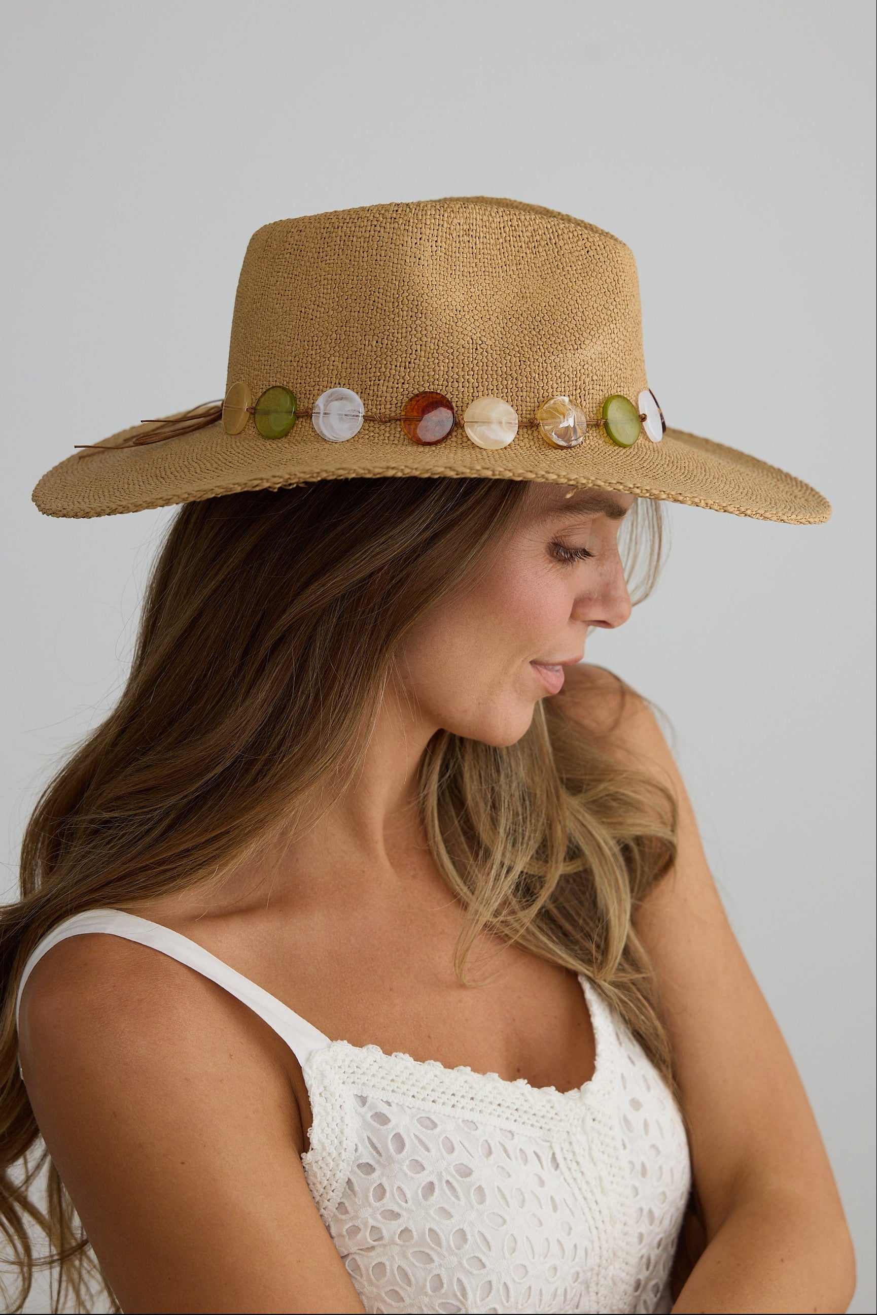 Woman wearing a straw hat with decorative stones on a plain background