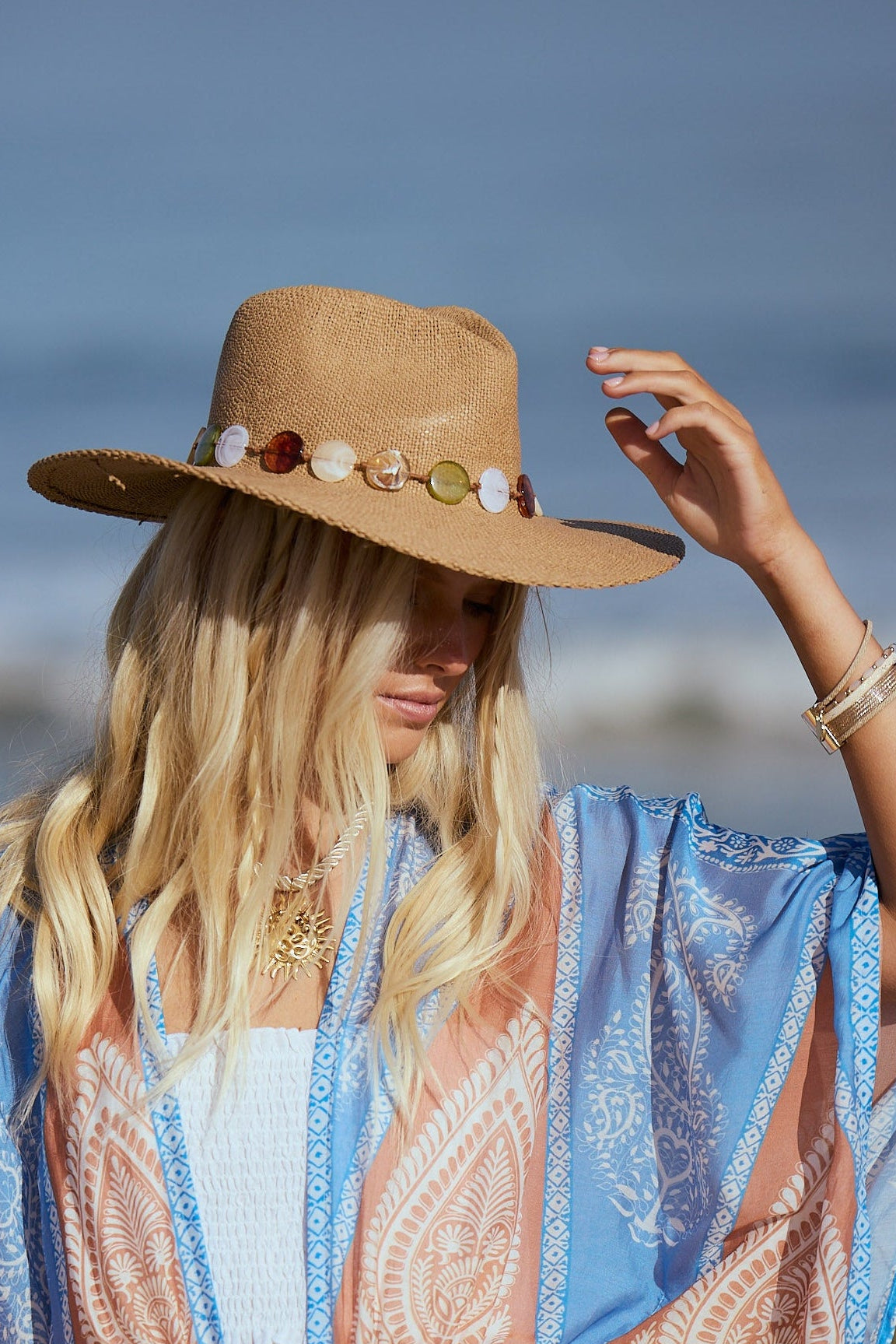 Woman on a beach wearing a wide-brimmed hat and a patterned scarf.