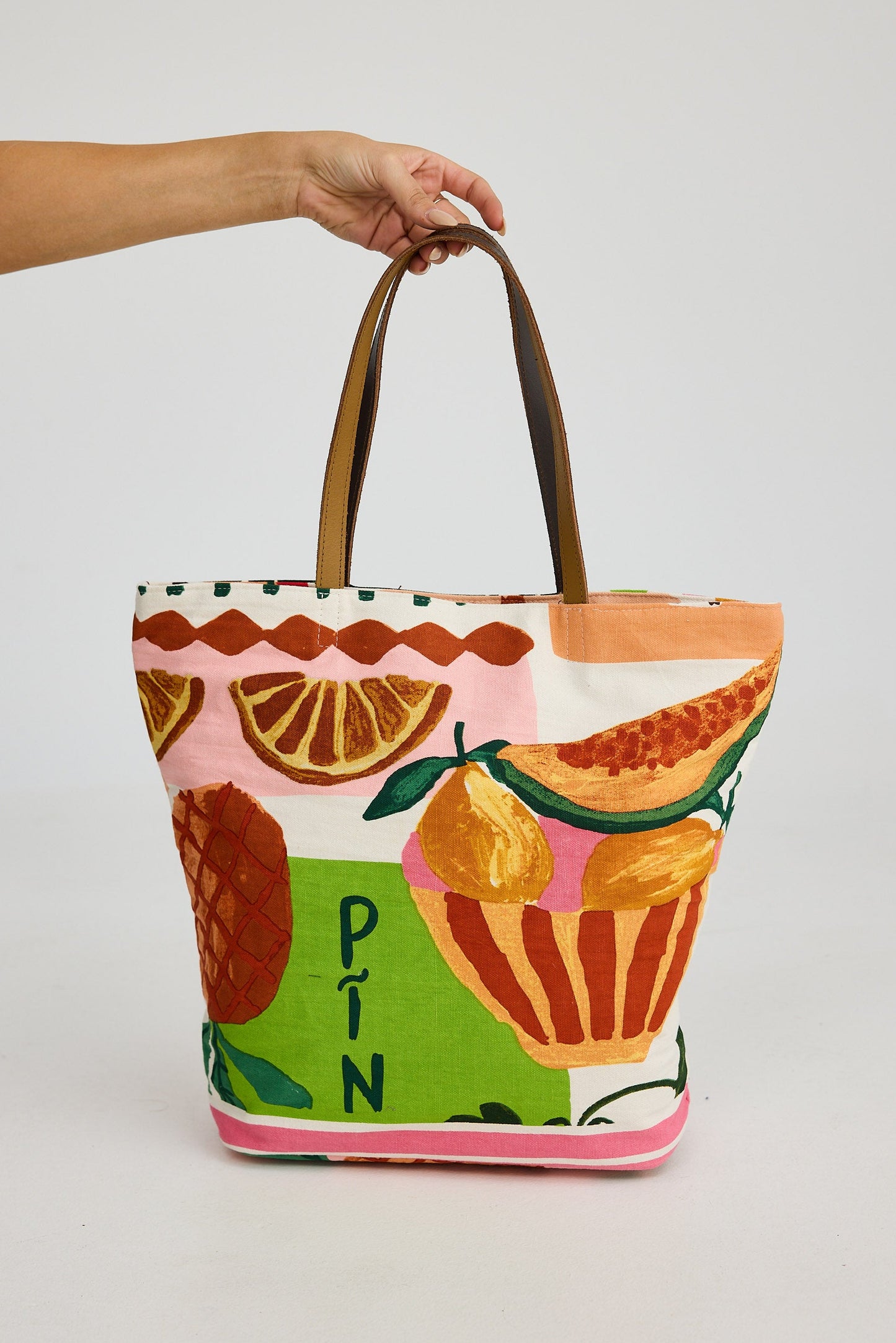 Tote bag with fruit design held by a hand on a white background