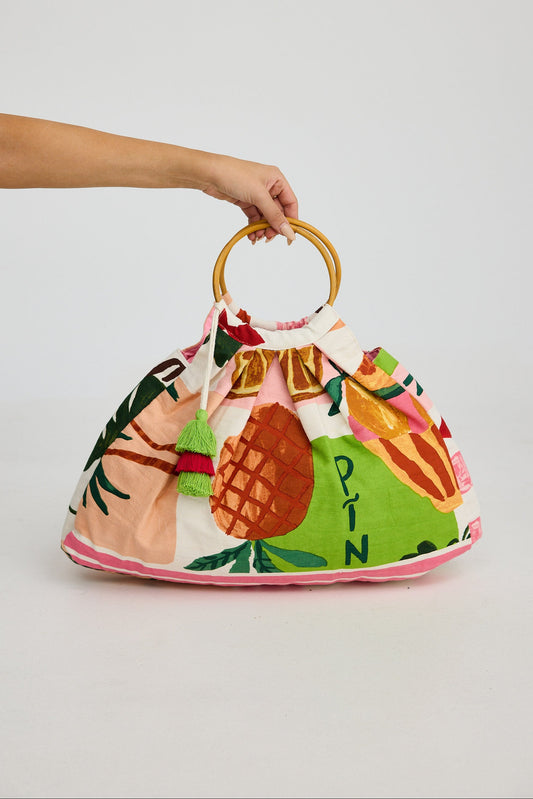 Handbag with tropical fruit design held by a person against a plain background