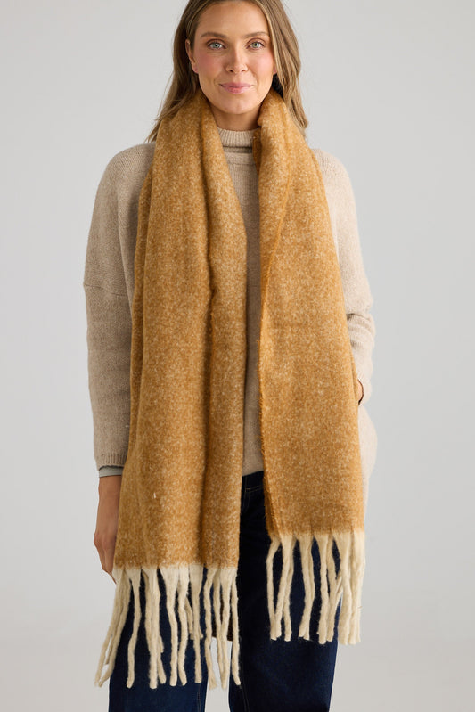 Woman wearing a brown scarf with white fringe on a gray background