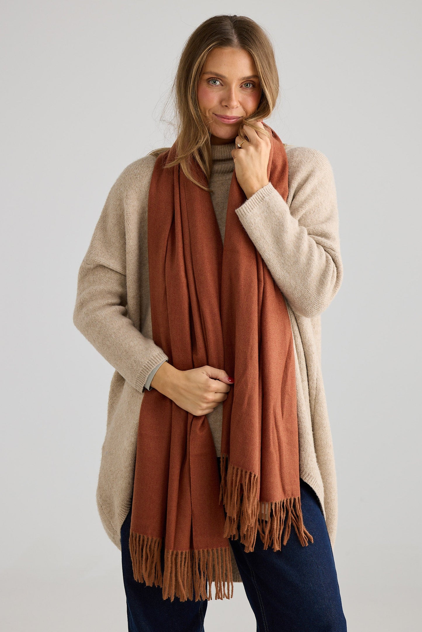 Woman wearing a beige knit and rust-colored scarf on a plain background