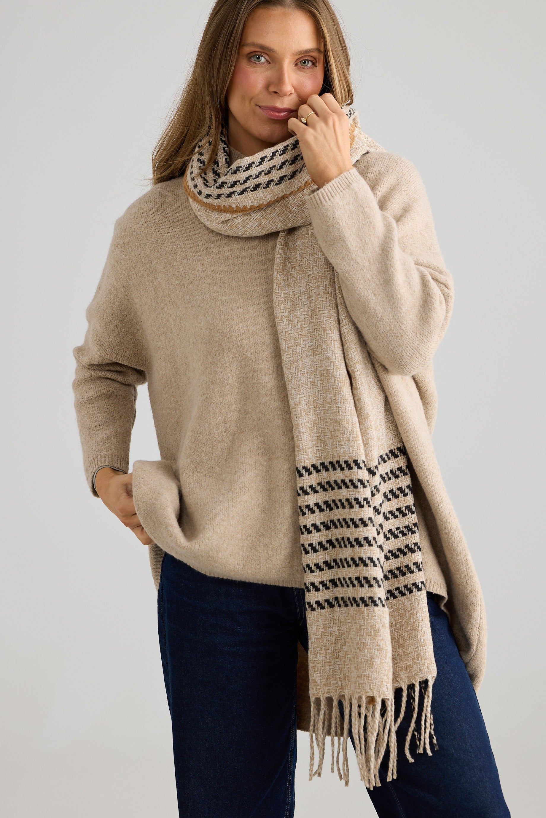 Woman wearing a beige sweater and patterned scarf against a plain background