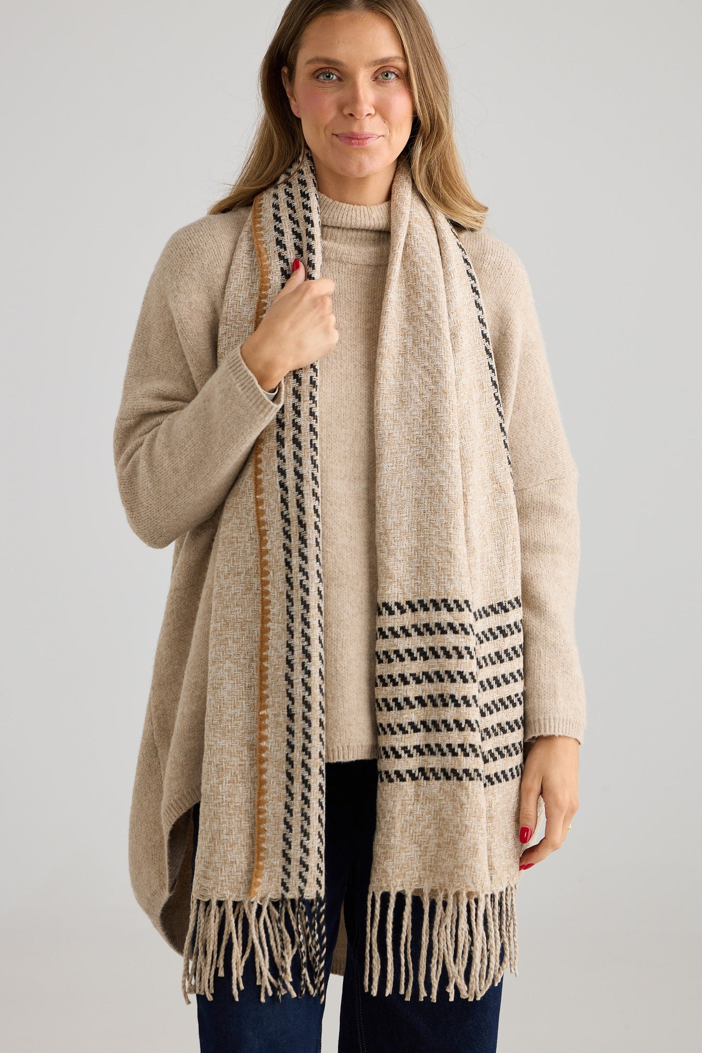 Woman wearing a beige knit and patterned scarf against a plain background