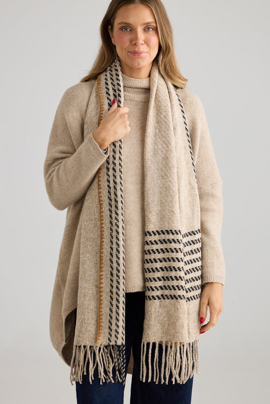 Woman wearing a beige knit and patterned scarf against a plain background