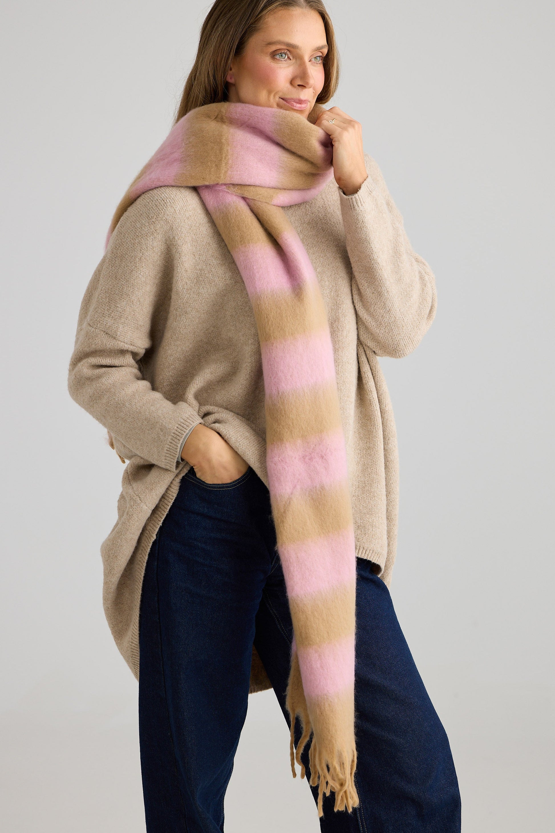 Woman wearing a large striped scarf in pink and tan on a plain background