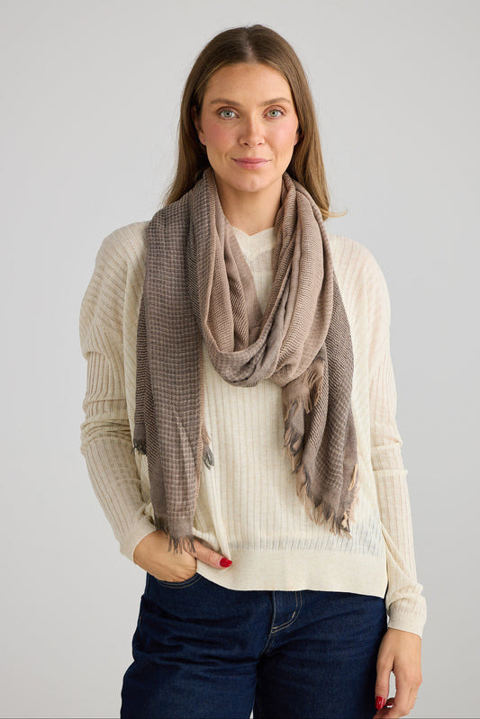 Woman wearing a beige sweater, blue jeans with a grey scarf on a plain background
