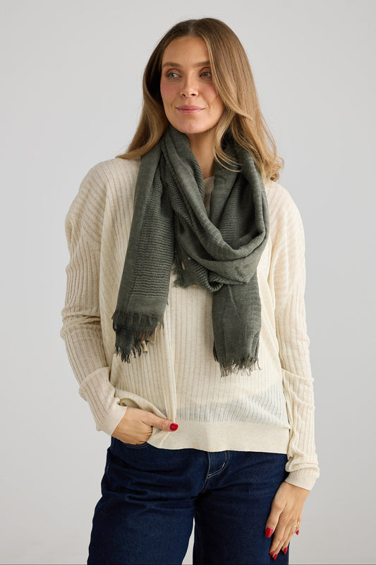Woman wearing a green scarf and beige sweater against a plain background