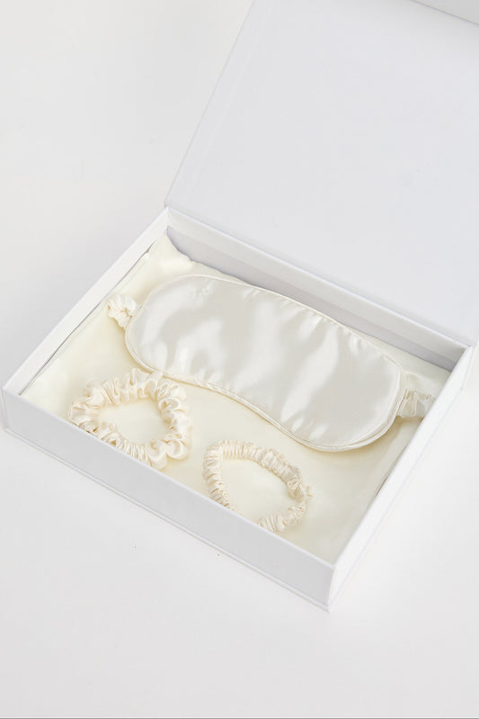 White satin eye mask in an open white box on a light gray background