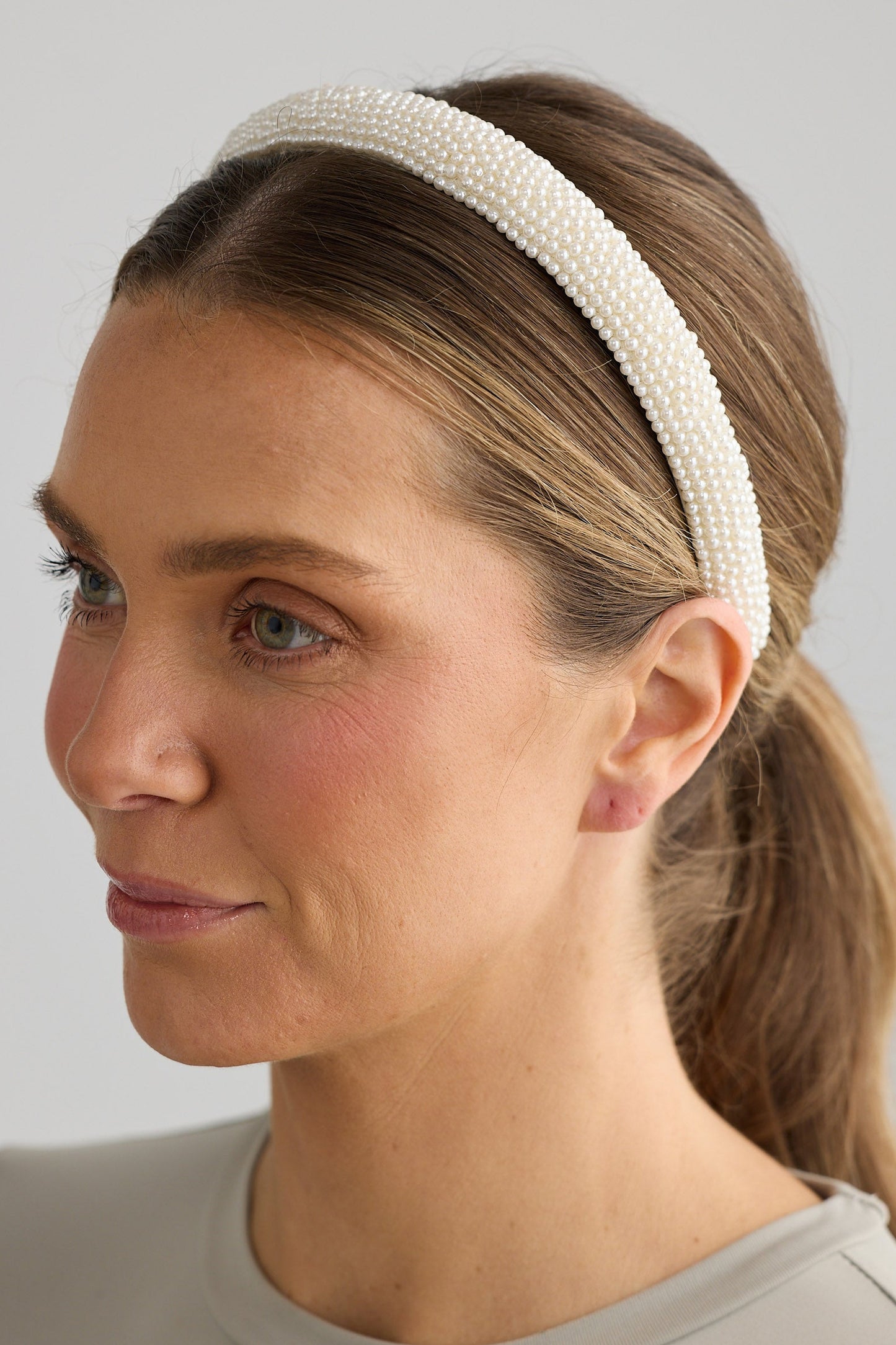 Woman wearing a beige headband against a plain background