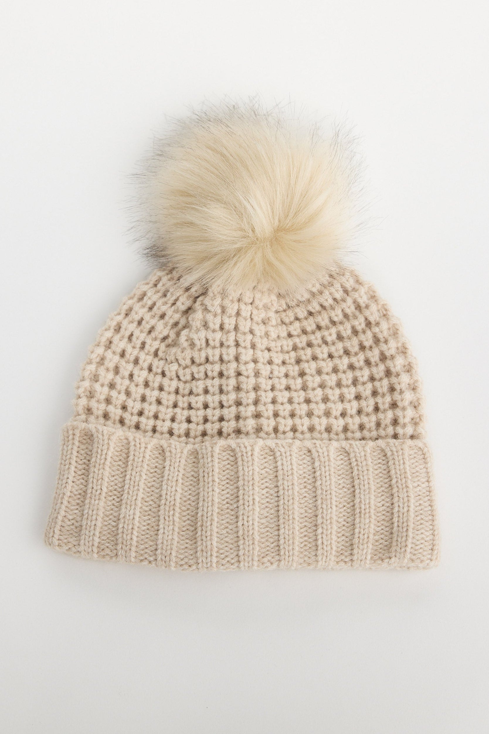 Beige knit beanie with a white pom-pom on a light gray background
