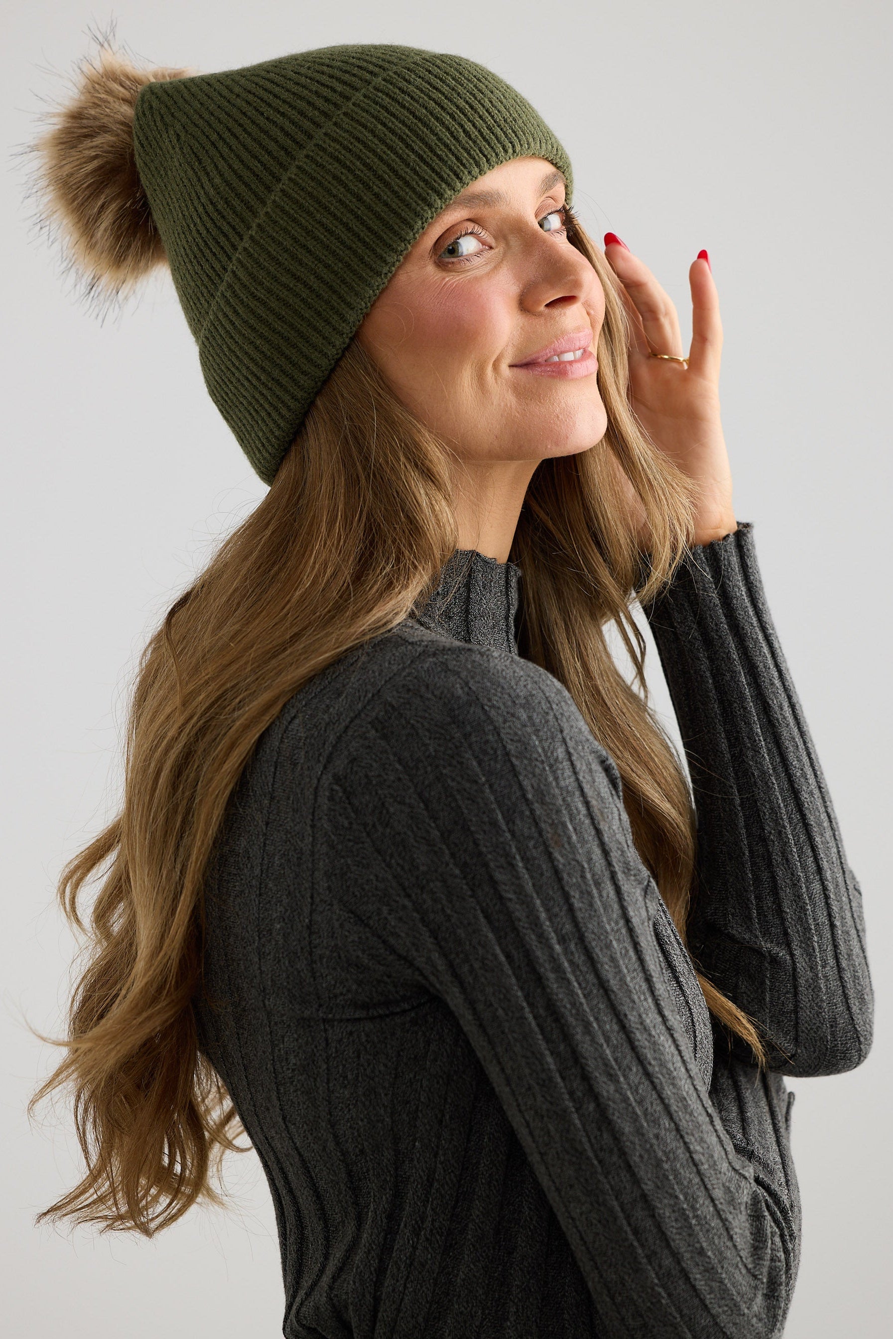 Woman wearing a green knit beanie with a pom-pom on a plain background