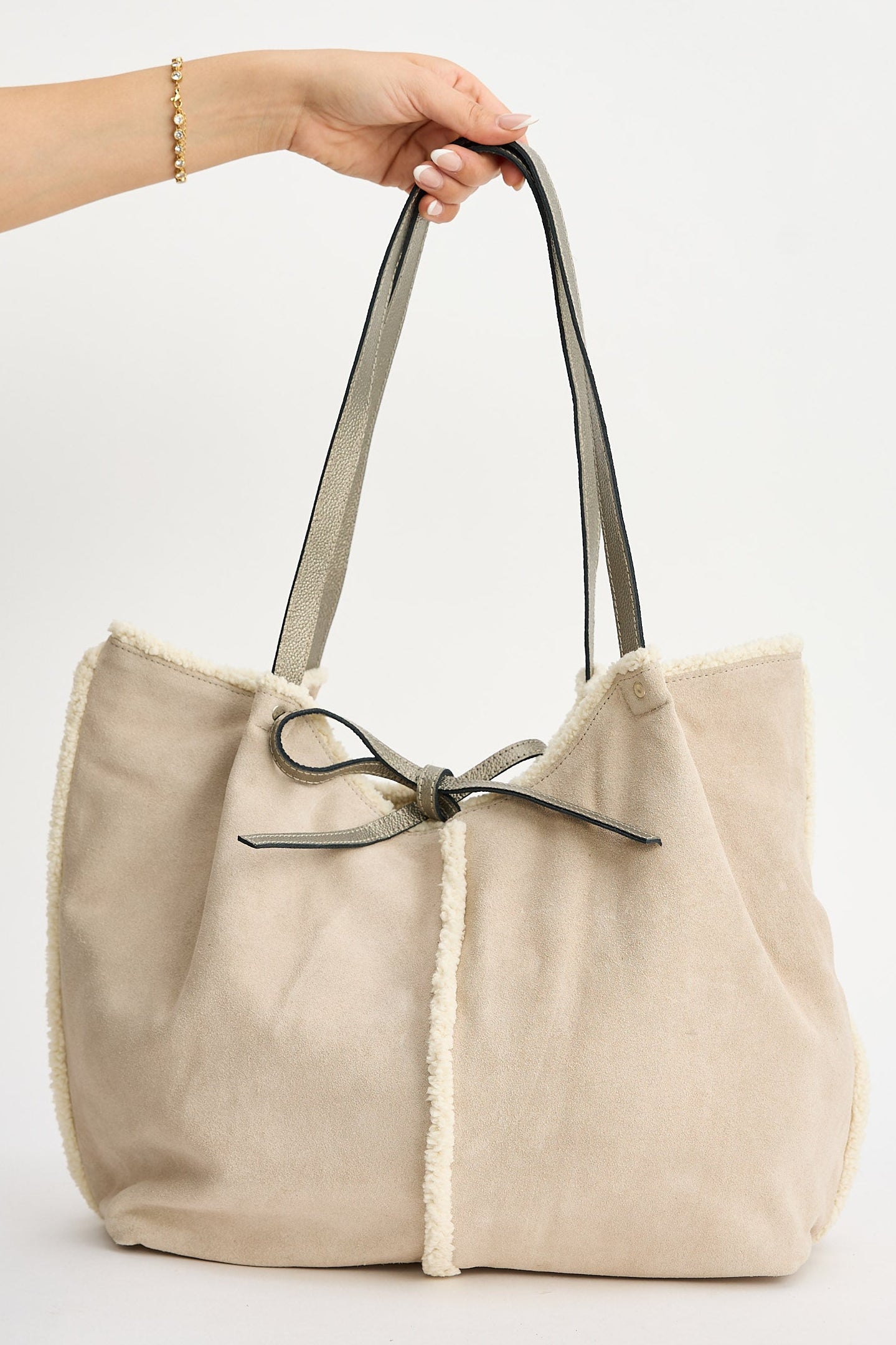 Beige tote bag with a bow held by a hand on a white background