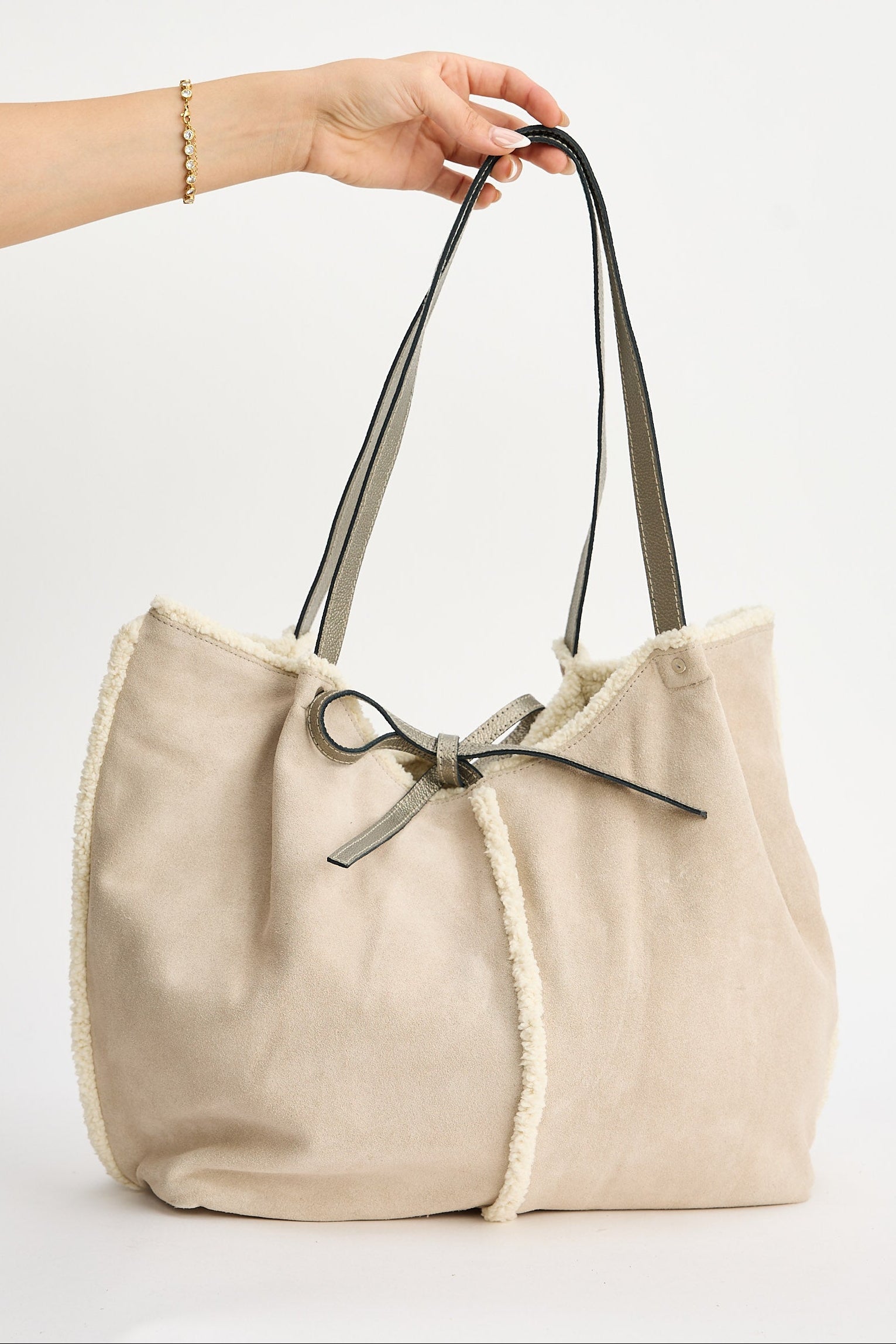 Beige tote bag with a bow held by a hand on a light gray background