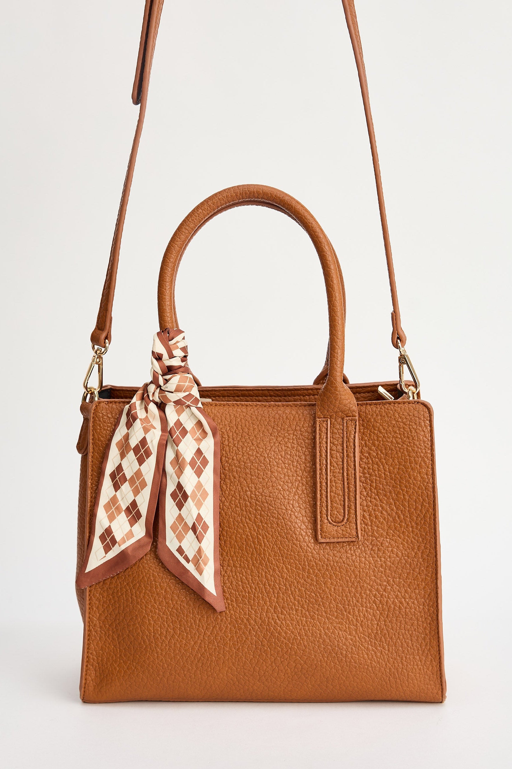 Brown handbag with a patterned scarf around the handle on a white background