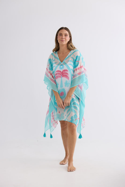 Model wearing Stella Kaftan in azure palm, front view. V-neckline, sheer drape and tasselled corners.