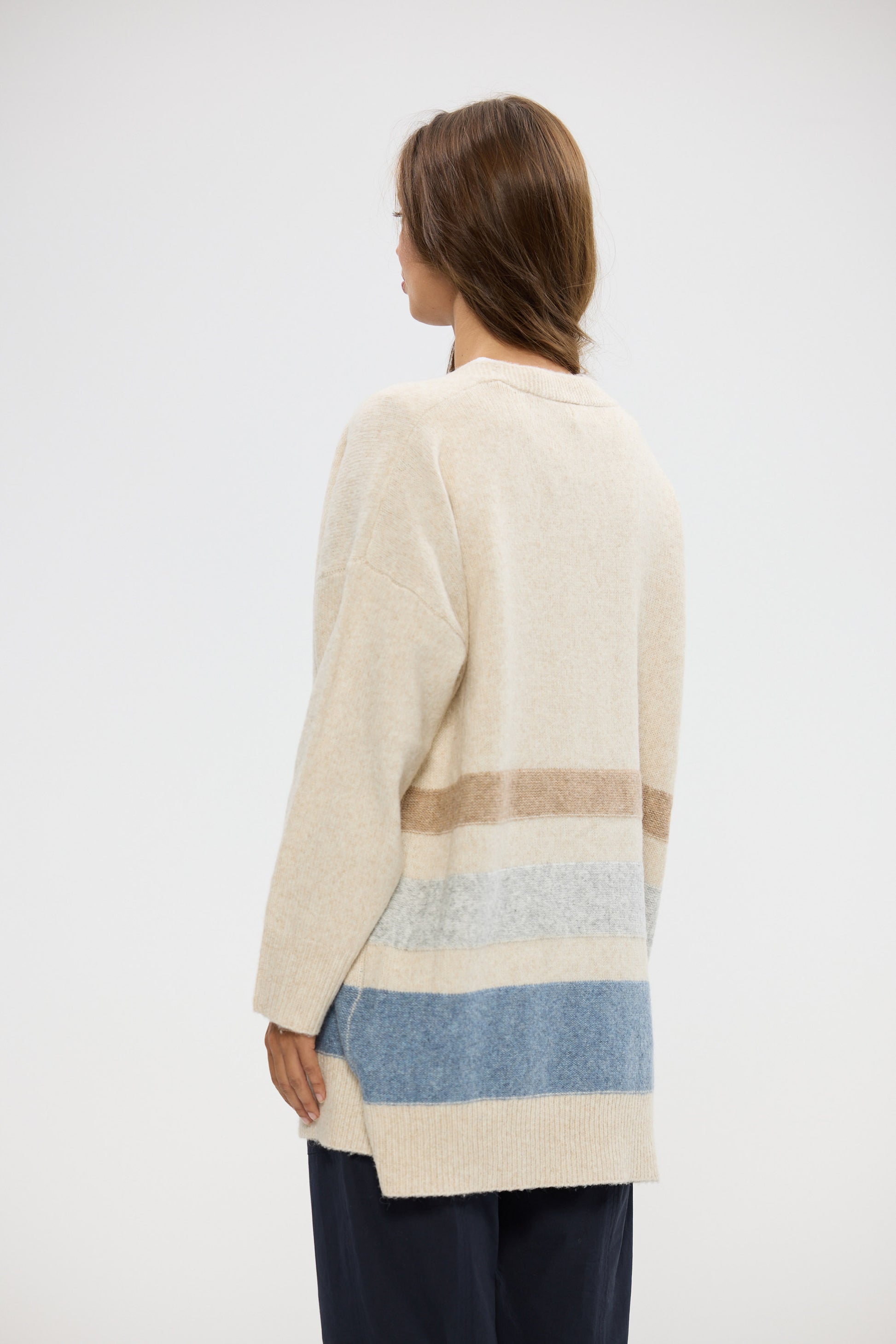 Woman wearing a long, light-colored cardigan with horizontal stripes on a white background