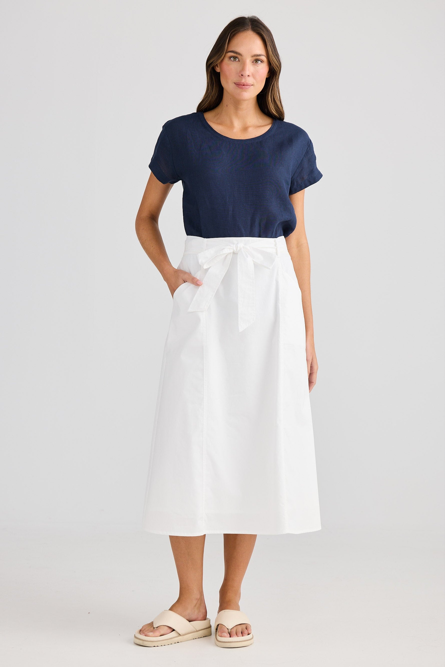 Woman wearing a navy top and white skirt on a light gray background
