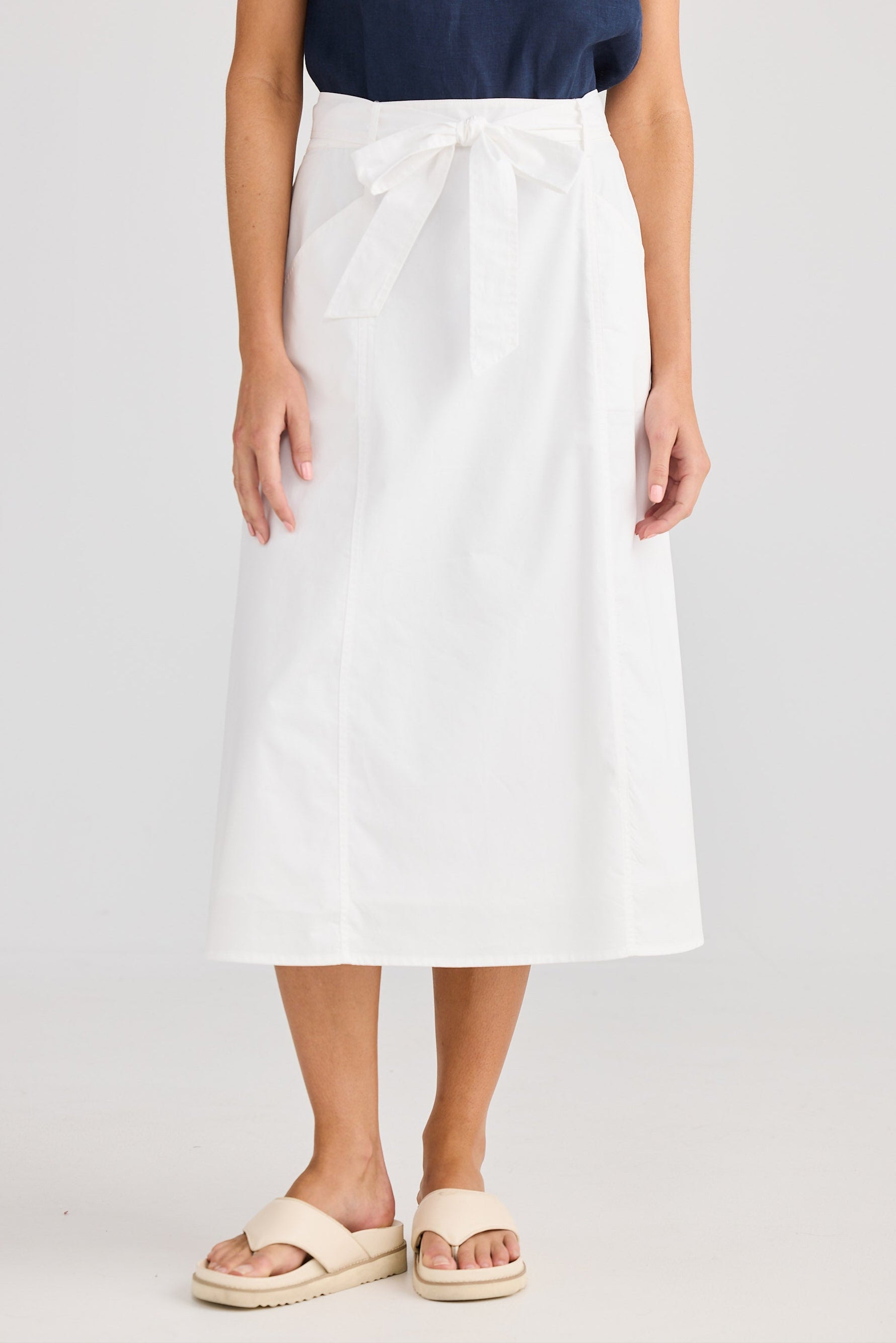Person wearing a white skirt and navy top on a plain background