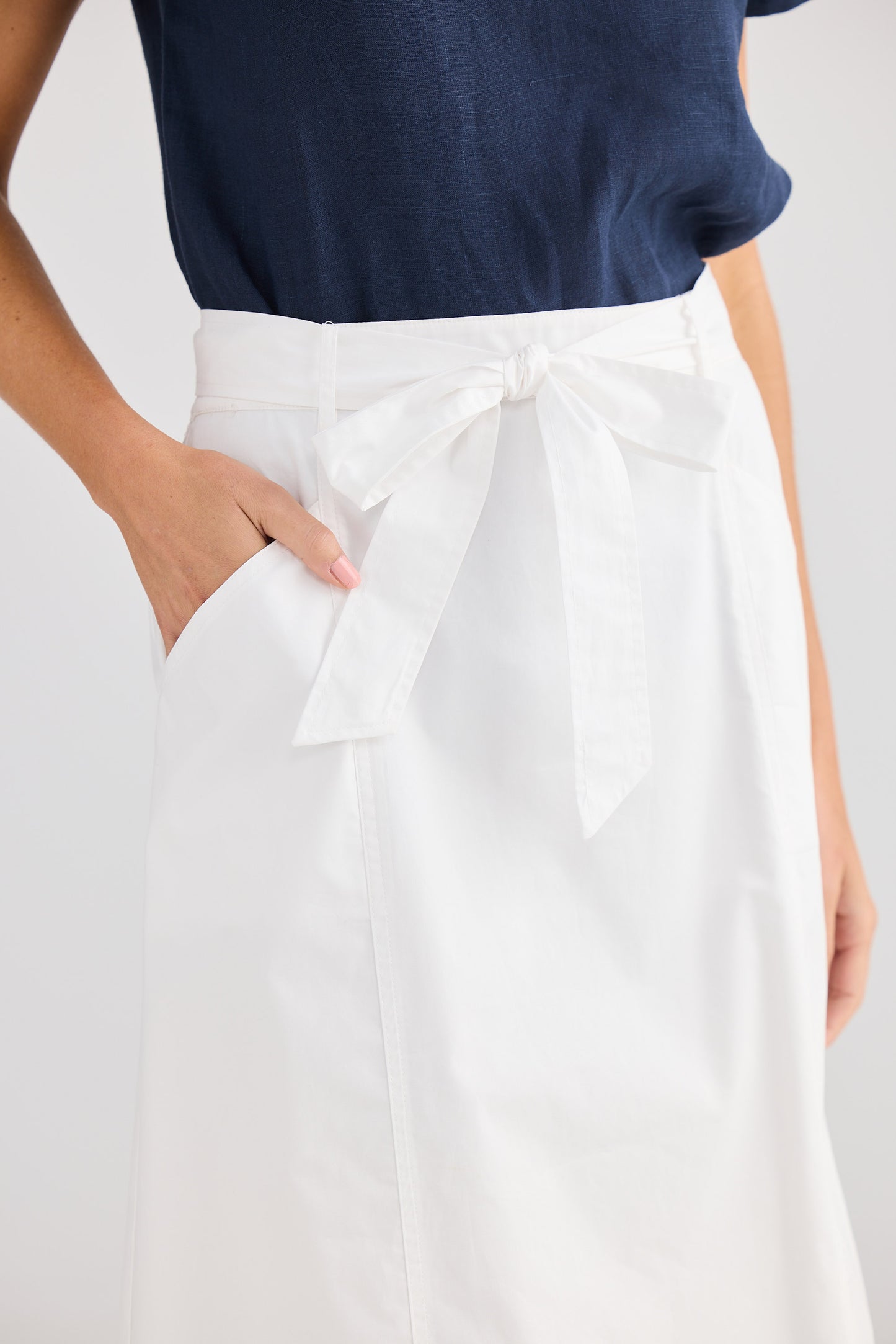 Person wearing a navy top and white pants with a bow detail on a light gray background